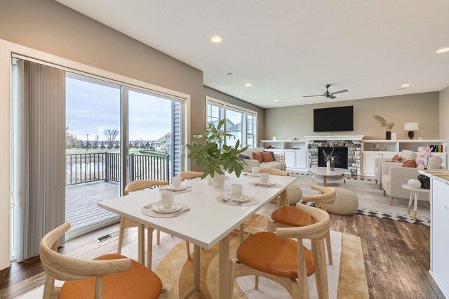 dining space featuring a ceiling fan, a water view, wood finished floors, and a fireplace