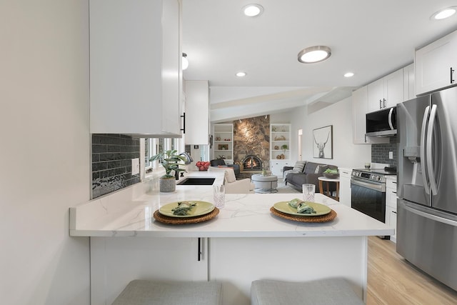 kitchen featuring white cabinets, stainless steel appliances, a breakfast bar, a sink, and a peninsula