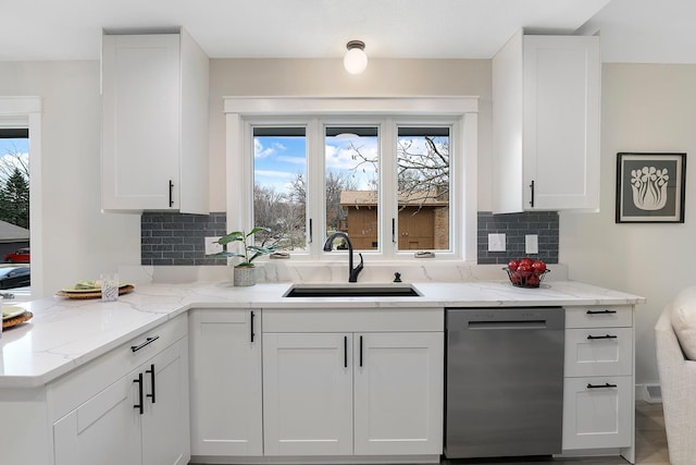 kitchen with white cabinets, stainless steel dishwasher, a sink, light stone countertops, and tasteful backsplash