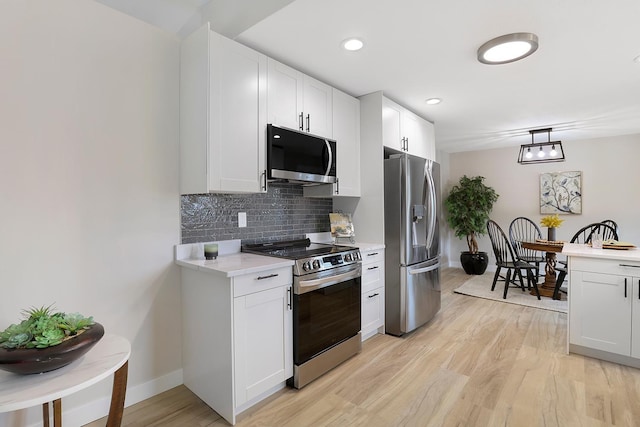 kitchen featuring stainless steel appliances, light wood-type flooring, baseboards, white cabinetry, and decorative backsplash