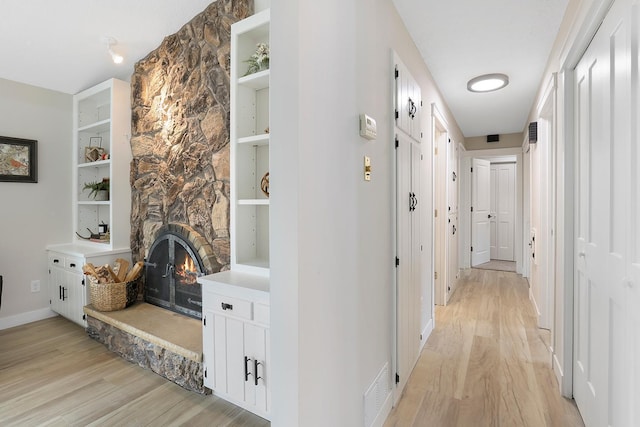 hall featuring baseboards, light wood-style flooring, visible vents, and built in shelves