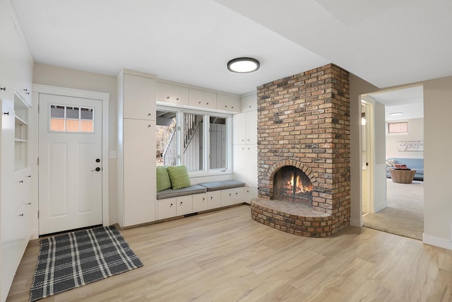 mudroom with baseboards, light wood-style flooring, and a brick fireplace