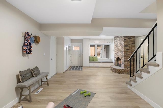 entrance foyer with light wood-style flooring, baseboards, a fireplace, and stairs