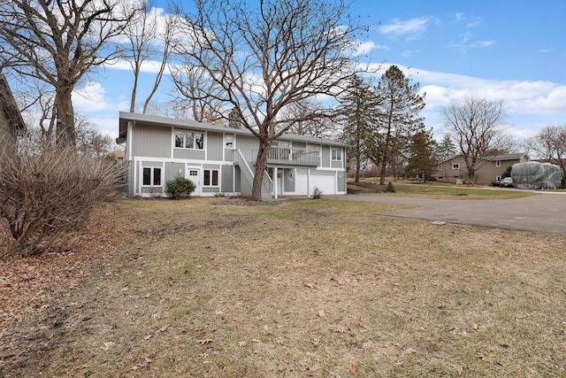 rear view of property with an attached garage, driveway, a yard, and stairway