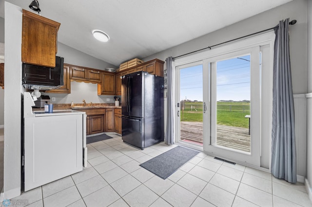 kitchen featuring freestanding refrigerator, lofted ceiling, brown cabinetry, range, and light tile patterned flooring