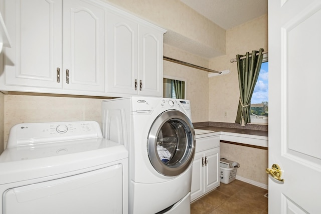 laundry room featuring tile patterned floors, baseboards, cabinet space, and washer and clothes dryer