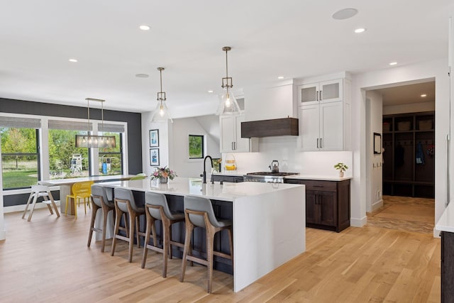 7450 73rd Ct N, Grant, MN 55082 - kitchen featuring a kitchen island with sink, light wood-style floors, a breakfast bar, recessed lighting, and glass insert cabinets