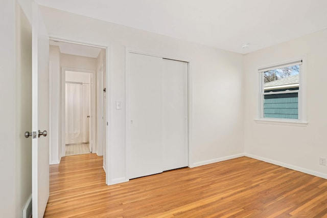 unfurnished bedroom featuring baseboards, light wood-type flooring, and a closet