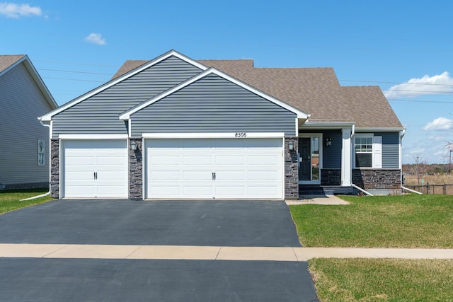 view of front of home featuring driveway, a front lawn, an attached garage, a shingled roof, and stone siding