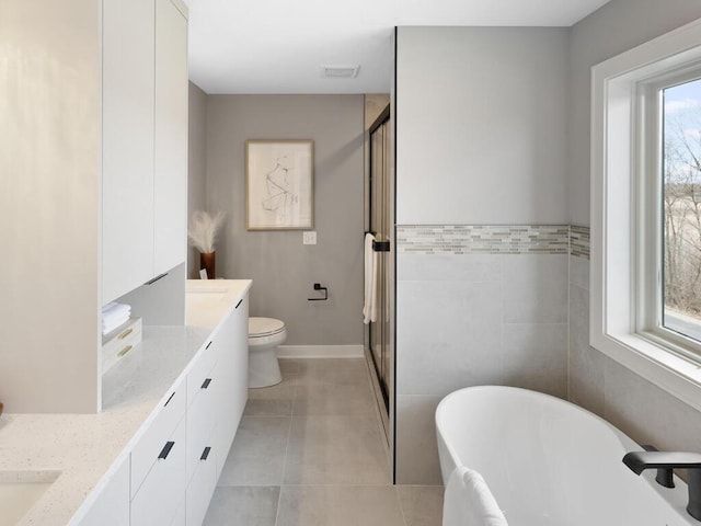 14913 Oakwood Dr, Burnsville, MN 55306 - full bathroom with tile patterned floors, a freestanding bath, double vanity, toilet, and a stall shower