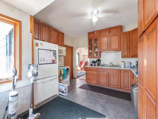 kitchen with a sink, glass insert cabinets, a ceiling fan, white appliances, and light countertops