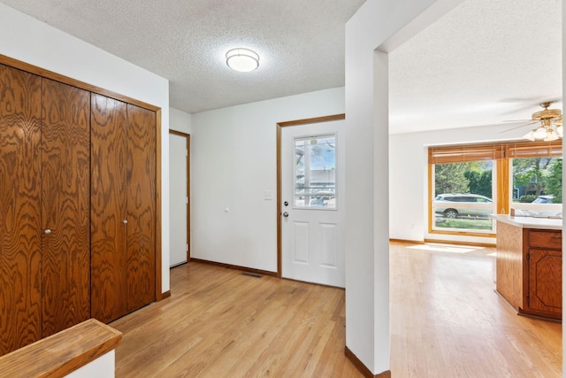foyer entrance with light wood-style floors, a textured ceiling, a ceiling fan, and baseboards