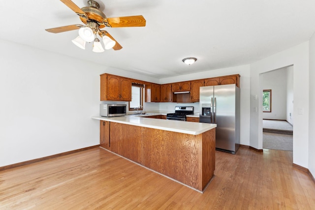 kitchen with stainless steel appliances, a peninsula, light countertops, light wood finished floors, and baseboards