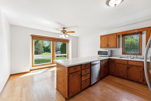 kitchen with a sink, stainless steel appliances, a peninsula, light countertops, and brown cabinets