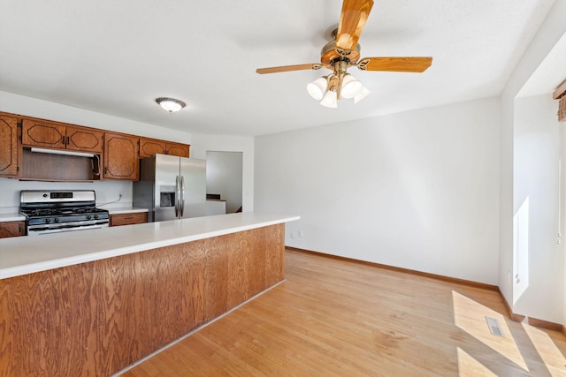 kitchen with stainless steel appliances, light countertops, light wood-type flooring, ceiling fan, and baseboards