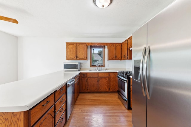 kitchen with appliances with stainless steel finishes, a sink, a peninsula, light wood finished floors, and brown cabinets