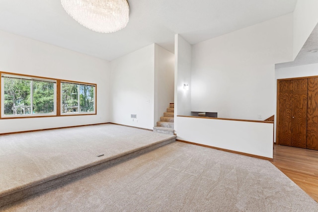 carpeted empty room with baseboards, stairs, and wood finished floors