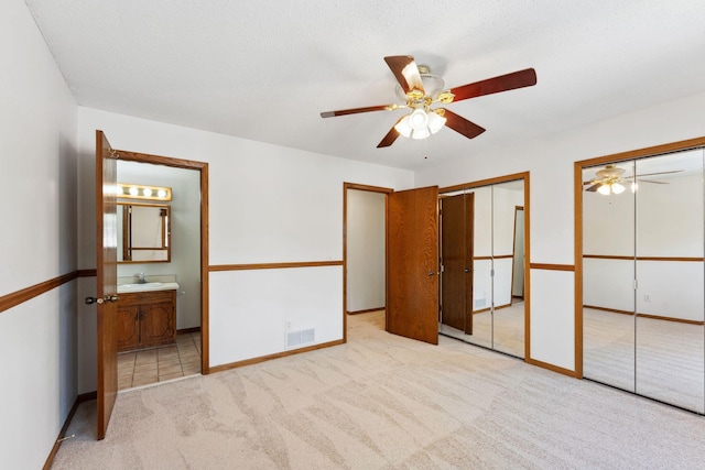 unfurnished bedroom featuring multiple closets, a sink, light carpet, connected bathroom, and baseboards