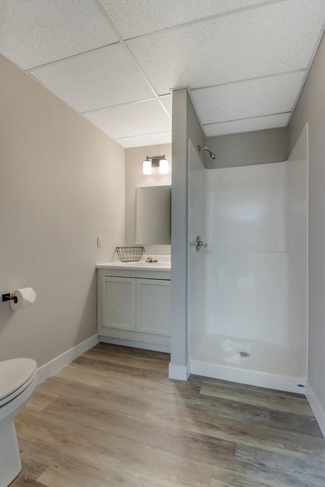bathroom featuring wood finished floors, toilet, vanity, a paneled ceiling, and a shower