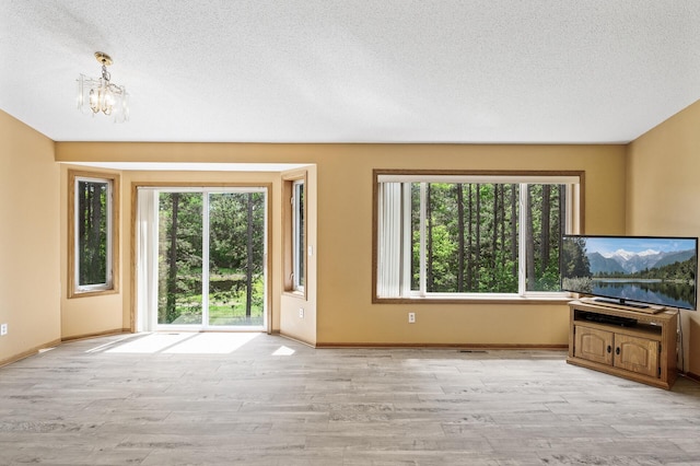17813 224th Ave NW, Big Lake, MN 55309 - unfurnished living room featuring light wood-type flooring, plenty of natural light, a textured ceiling, and a chandelier