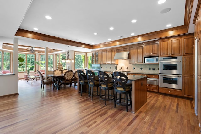 4325 Trillium Ln W, Minnetrista, MN 55364 - kitchen featuring stainless steel appliances, brown cabinets, a breakfast bar area, ornamental molding, and an island with sink