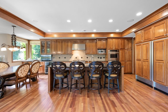 4325 Trillium Ln W, Minnetrista, MN 55364 - kitchen featuring appliances with stainless steel finishes, a tray ceiling, brown cabinets, under cabinet range hood, and ornamental molding