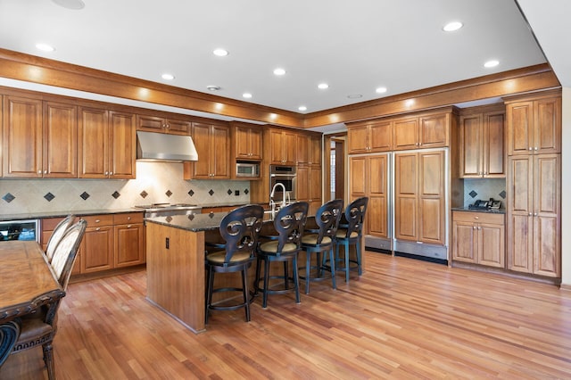 4325 Trillium Ln W, Minnetrista, MN 55364 - kitchen featuring under cabinet range hood, brown cabinetry, built in appliances, light wood-style flooring, and recessed lighting