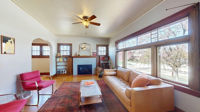 living room featuring crown molding, a fireplace, a ceiling fan, and wood finished floors