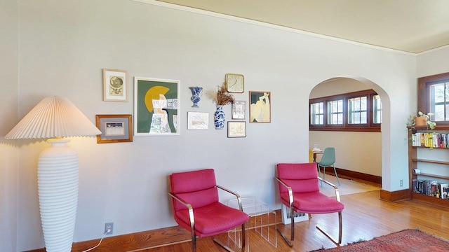 sitting room featuring baseboards, arched walkways, crown molding, and wood finished floors