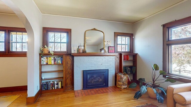 living room with ornamental molding, a brick fireplace, wood finished floors, baseboards, and arched walkways