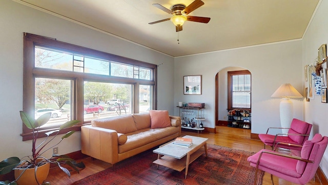 living room featuring ceiling fan, crown molding, arched walkways, wood finished floors, and baseboards
