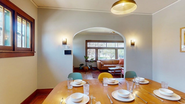dining room featuring arched walkways, baseboards, ornamental molding, and wood finished floors