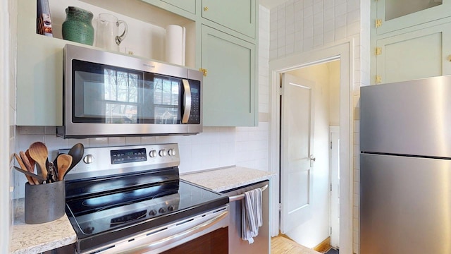 kitchen with green cabinetry, light stone counters, tasteful backsplash, and stainless steel appliances