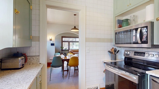 kitchen featuring backsplash, visible vents, appliances with stainless steel finishes, arched walkways, and light stone countertops