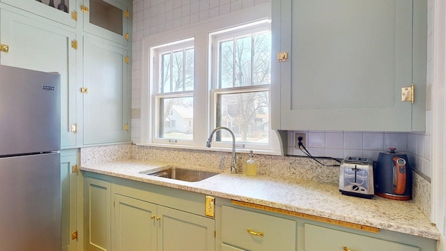 kitchen with freestanding refrigerator, a sink, green cabinets, and tasteful backsplash