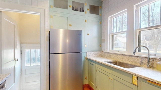 kitchen featuring a sink, glass insert cabinets, freestanding refrigerator, and a wealth of natural light