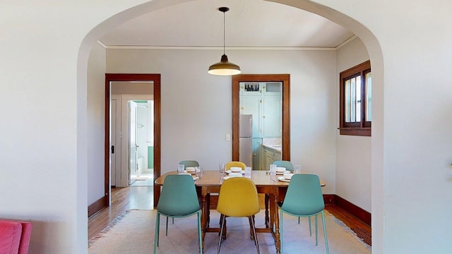 dining area with crown molding, arched walkways, baseboards, and light wood-type flooring