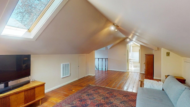 additional living space with visible vents, baseboards, vaulted ceiling with skylight, and hardwood / wood-style floors