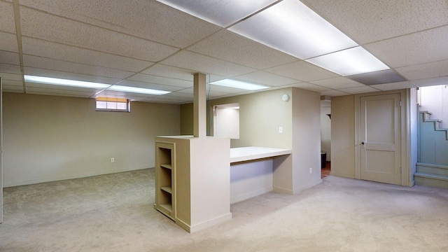 basement featuring baseboards, a drop ceiling, and light carpet