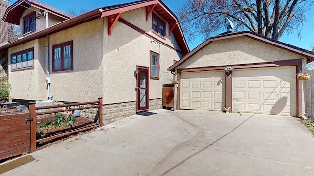 view of side of home featuring an attached garage, stucco siding, driveway, and fence