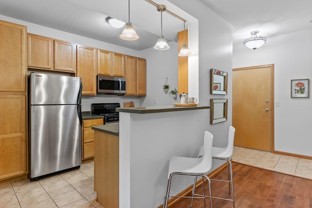 2565 Franklin Ave Unit 109, Saint Paul, MN 55114 - kitchen featuring stainless steel appliances, dark countertops, light tile patterned flooring, a peninsula, and decorative light fixtures