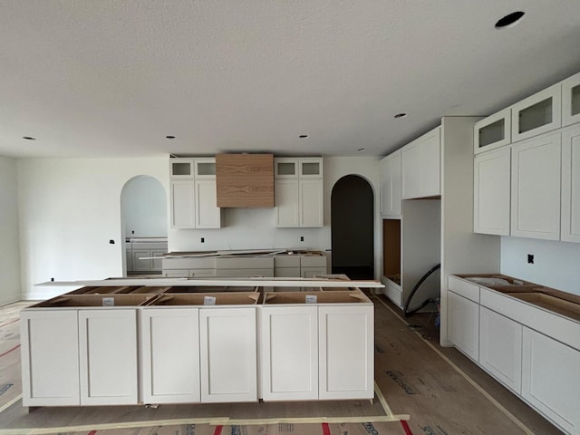 6200 Harkness Alcove S, Cottage Grove, MN 55016 - kitchen with arched walkways, a kitchen island, white cabinetry, a textured ceiling, and glass insert cabinets