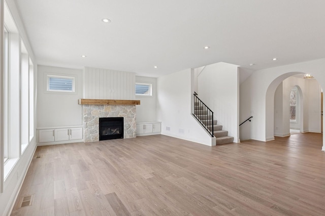 6200 Harkness Alcove S, Cottage Grove, MN 55016 - unfurnished living room featuring light wood-style flooring, arched walkways, stairs, a stone fireplace, and recessed lighting