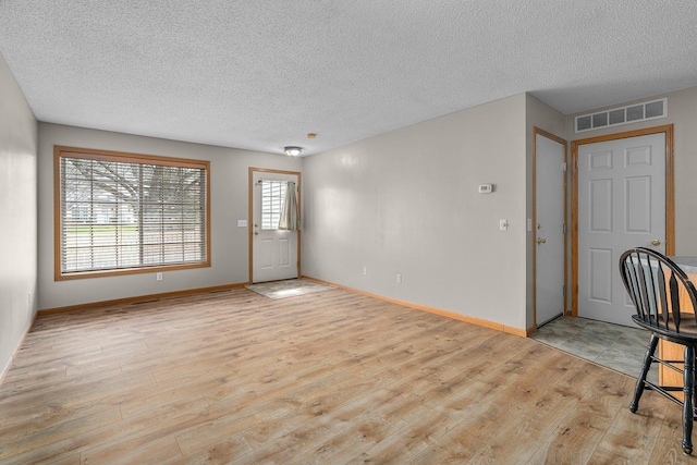 unfurnished living room with a textured ceiling, visible vents, light wood finished floors, and baseboards