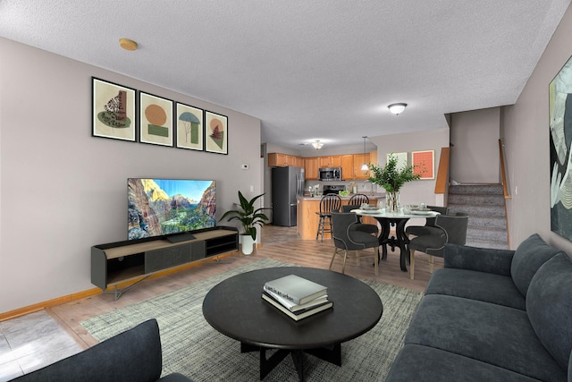 living room featuring light wood-type flooring, baseboards, a textured ceiling, and stairs