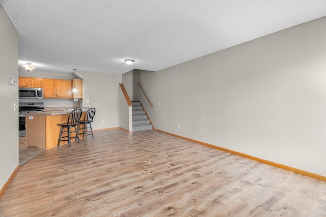 living area featuring stairway, baseboards, a textured ceiling, and light wood finished floors