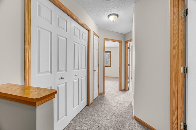 corridor with carpet floors, a textured ceiling, and baseboards
