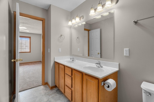full bathroom with toilet, a sink, double vanity, and a textured ceiling
