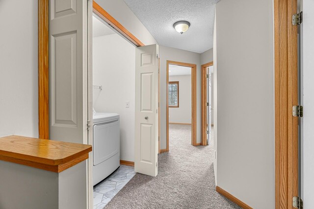 clothes washing area with baseboards, a textured ceiling, laundry area, and light carpet