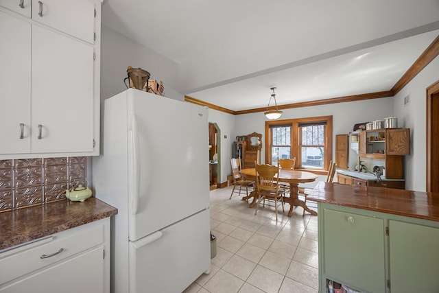 1114 6th St, Mankato, MN 56001 - kitchen with freestanding refrigerator, light tile patterned floors, backsplash, white cabinetry, and crown molding